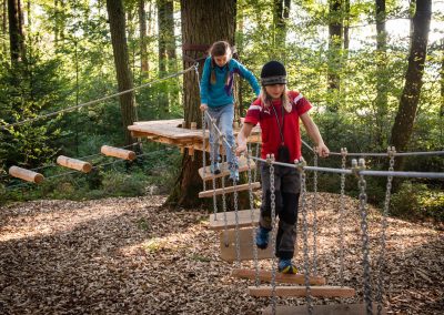 Kinder begehen eine Brücke auf einem Waldspielplatz