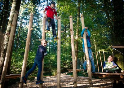Three children climbing on wooden poles in a forest playground