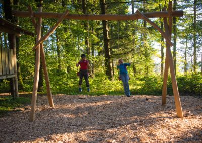 Kinder schaukeln auf einer Holzschaukel in einem neu gebauten Waldspielplatz
